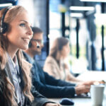 female-customer-support-operator-with-headset-smiling-with-collegues-background